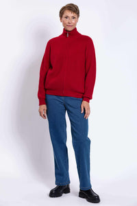 Woman in a red cardigan sweater, blue jeans, and black boots, posing against white background