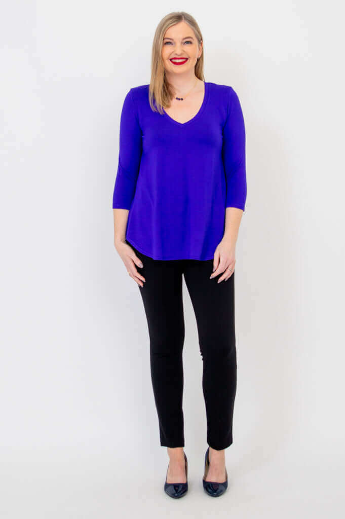 Woman standing in sapphire blue V-neck bamboo top and black pants