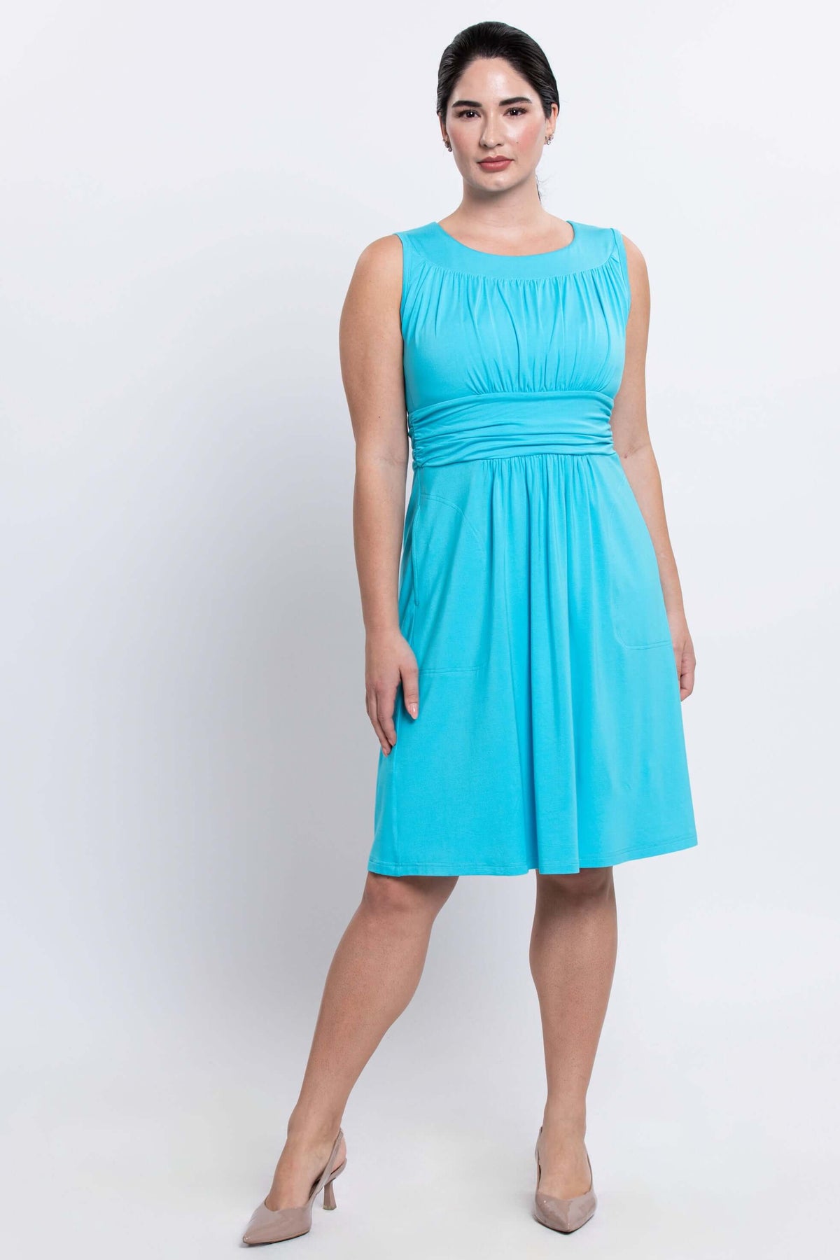 Woman wearing sleeveless aqua blue dress with ruched bodice and fitted waistband