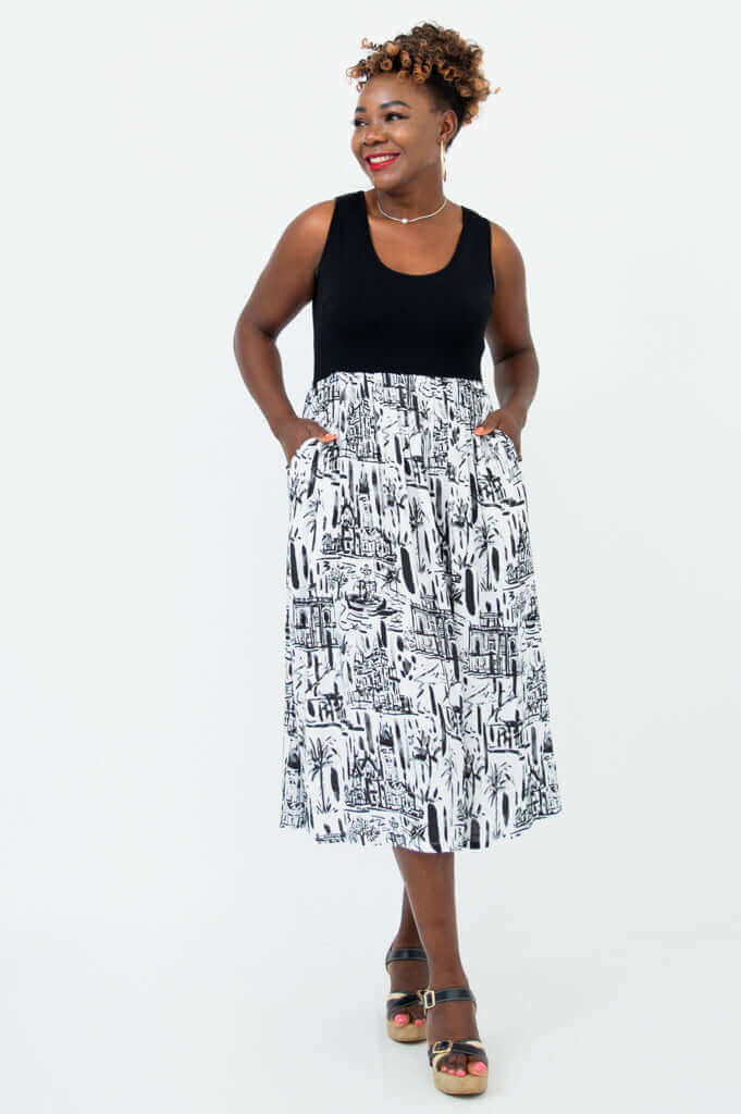Woman wearing a sleeveless black and white midi dress with an artistic city print and pockets