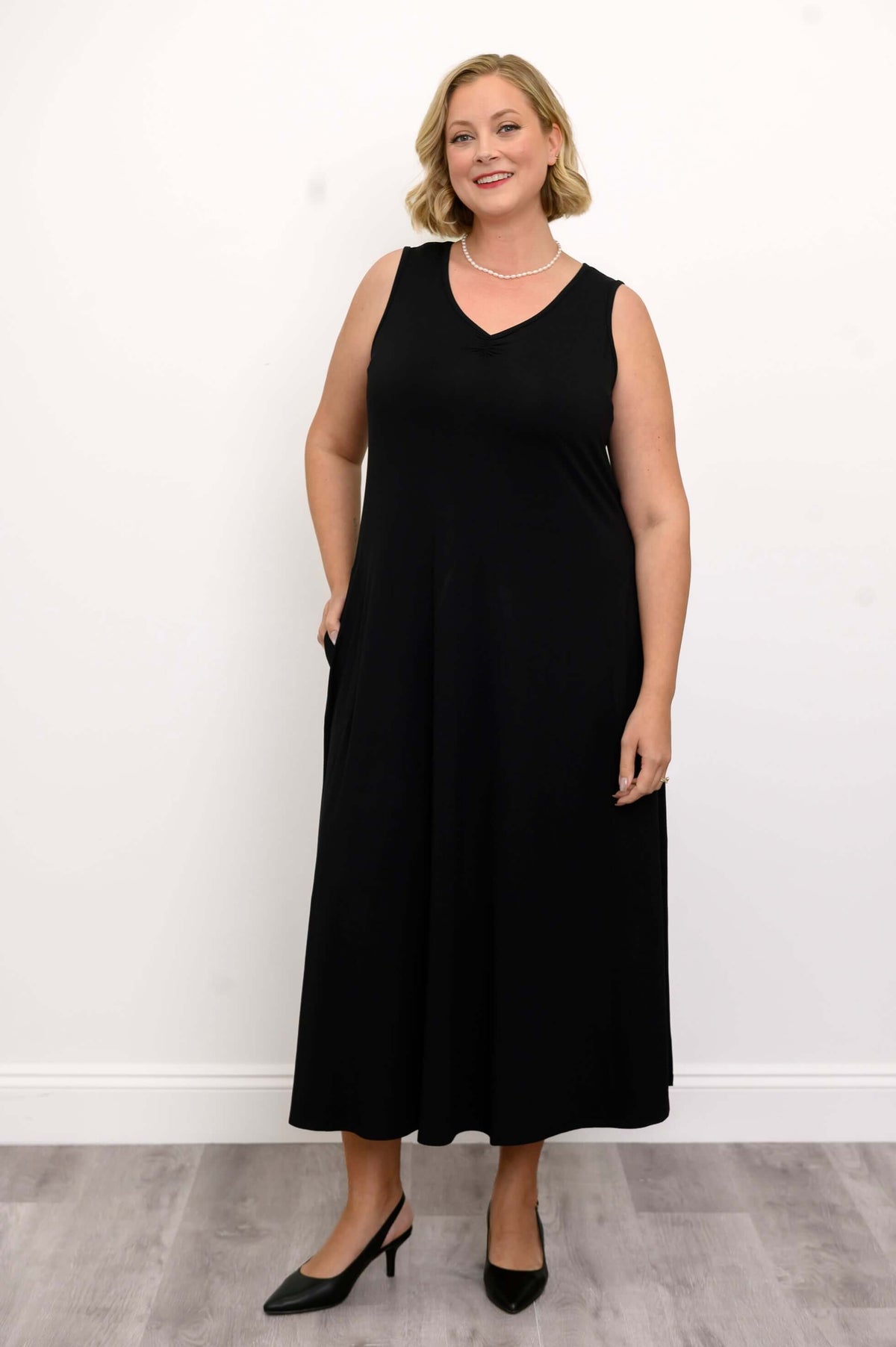 Woman wearing a sleeveless black maxi dress with a ruched V-neck, facing forward
