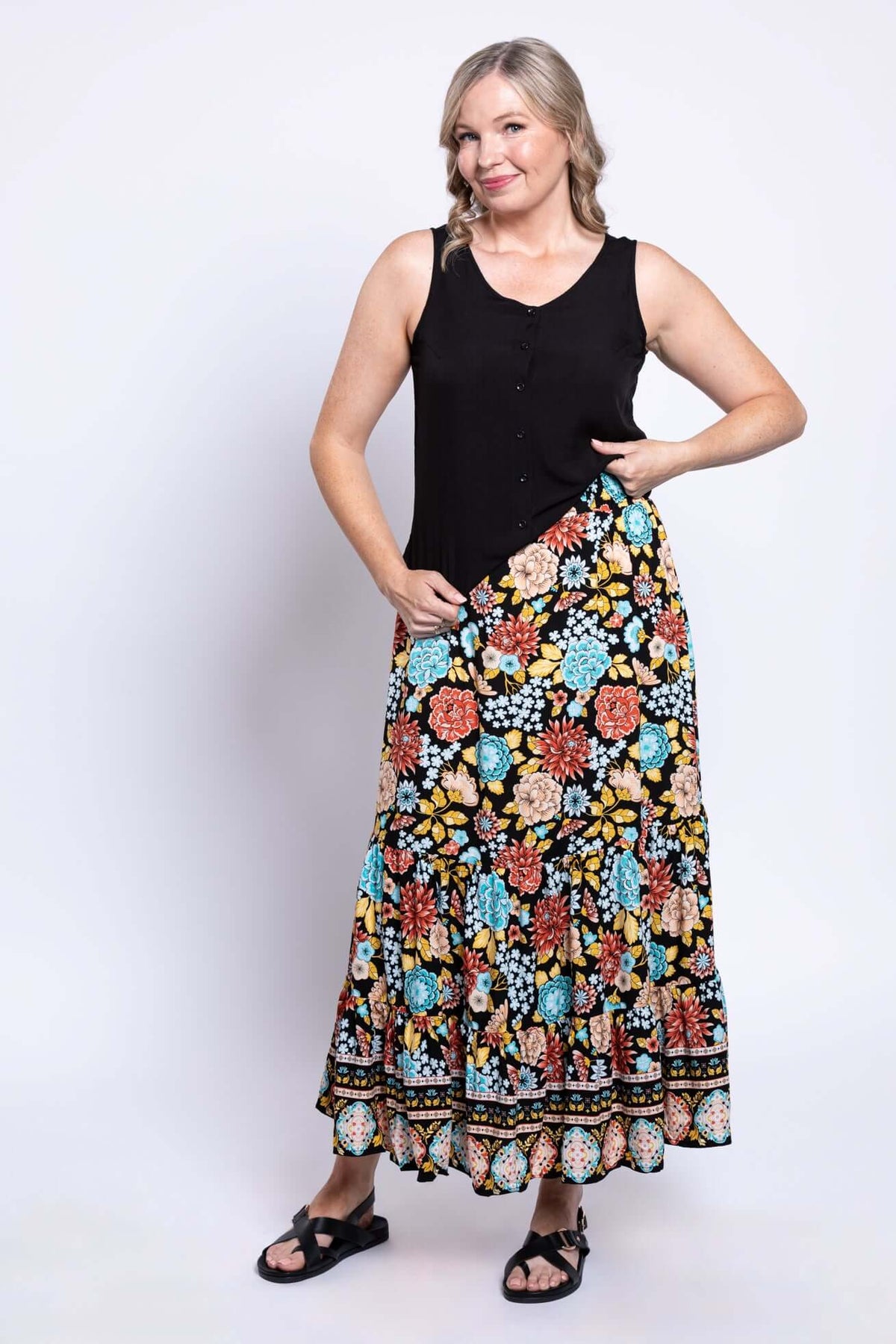 Smiling woman posing in a sleeveless black top and bold floral print maxi skirt