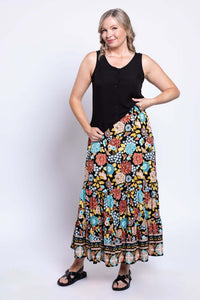 Smiling woman posing in a sleeveless black top and bold floral print maxi skirt
