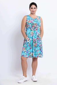 Woman in sleeveless blue floral dress with pockets standing in white sneakers