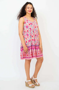 Woman in a sleeveless, pink and floral tiered dress, standing at a slight angle and smiling.