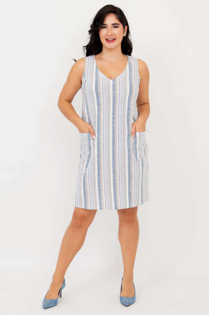 Woman wearing a sleeveless blue and white striped shift dress with V-neck and pockets