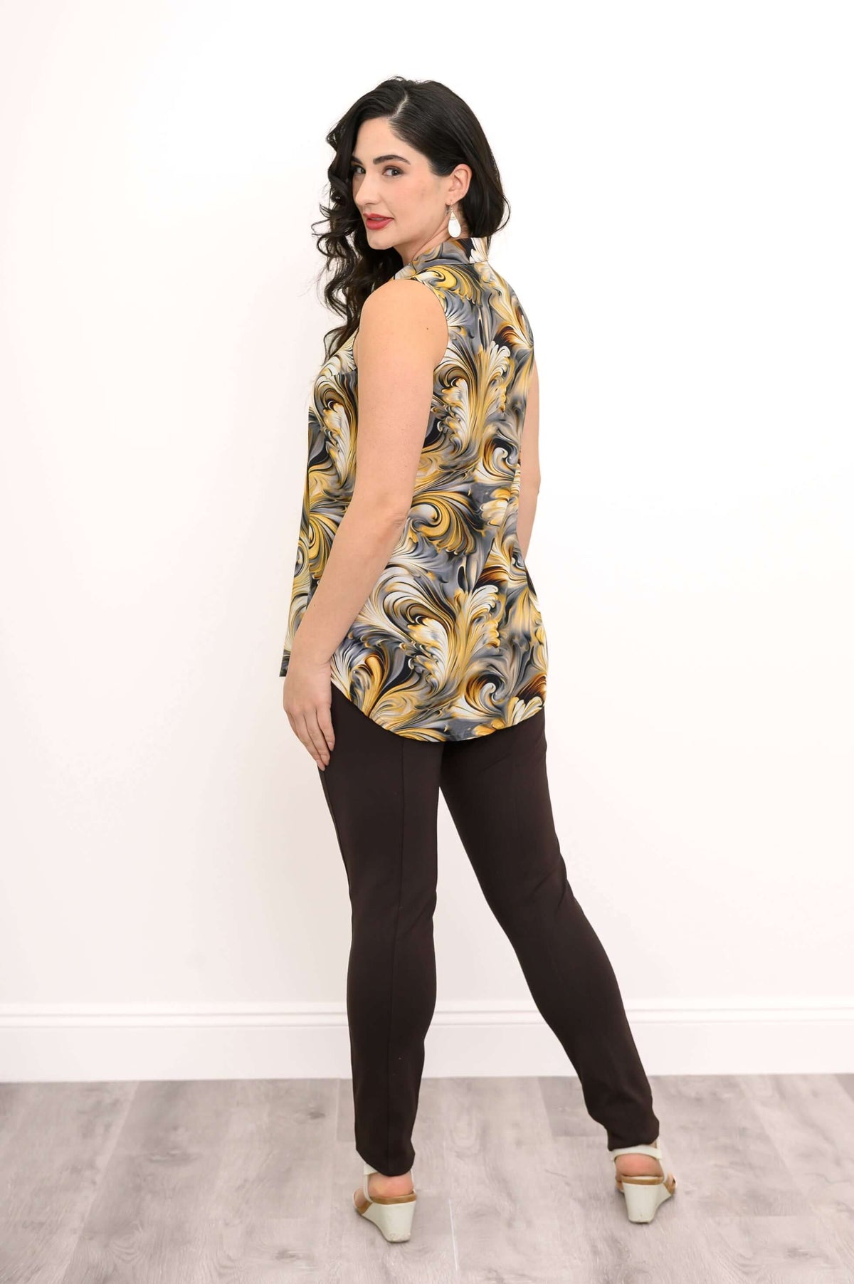 Woman looking over shoulder wearing sleeveless gold and gray swirl tank and dark pants