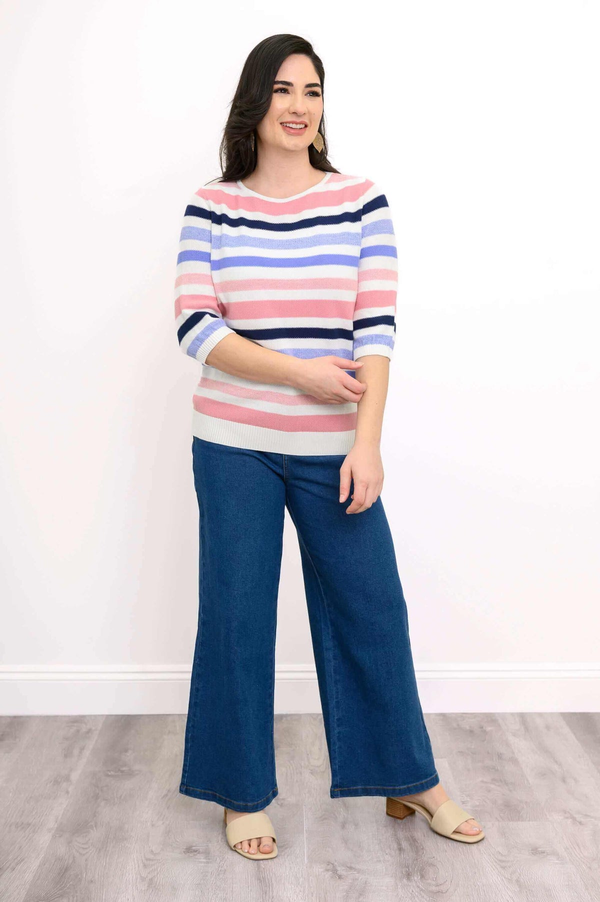 Woman wearing a colorful striped sweater with blue wide-leg jeans and beige sandals