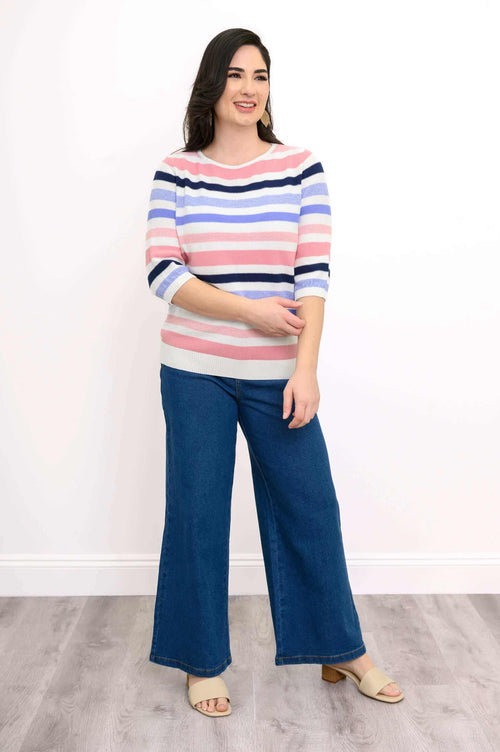 Woman wearing a colorful striped sweater with blue wide-leg jeans and beige sandals