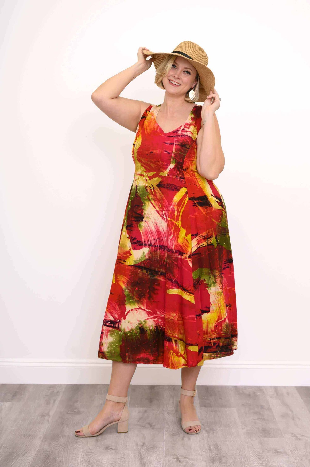 Woman in sunset-inspired abstract midi dress smiling and holding a sunhat
