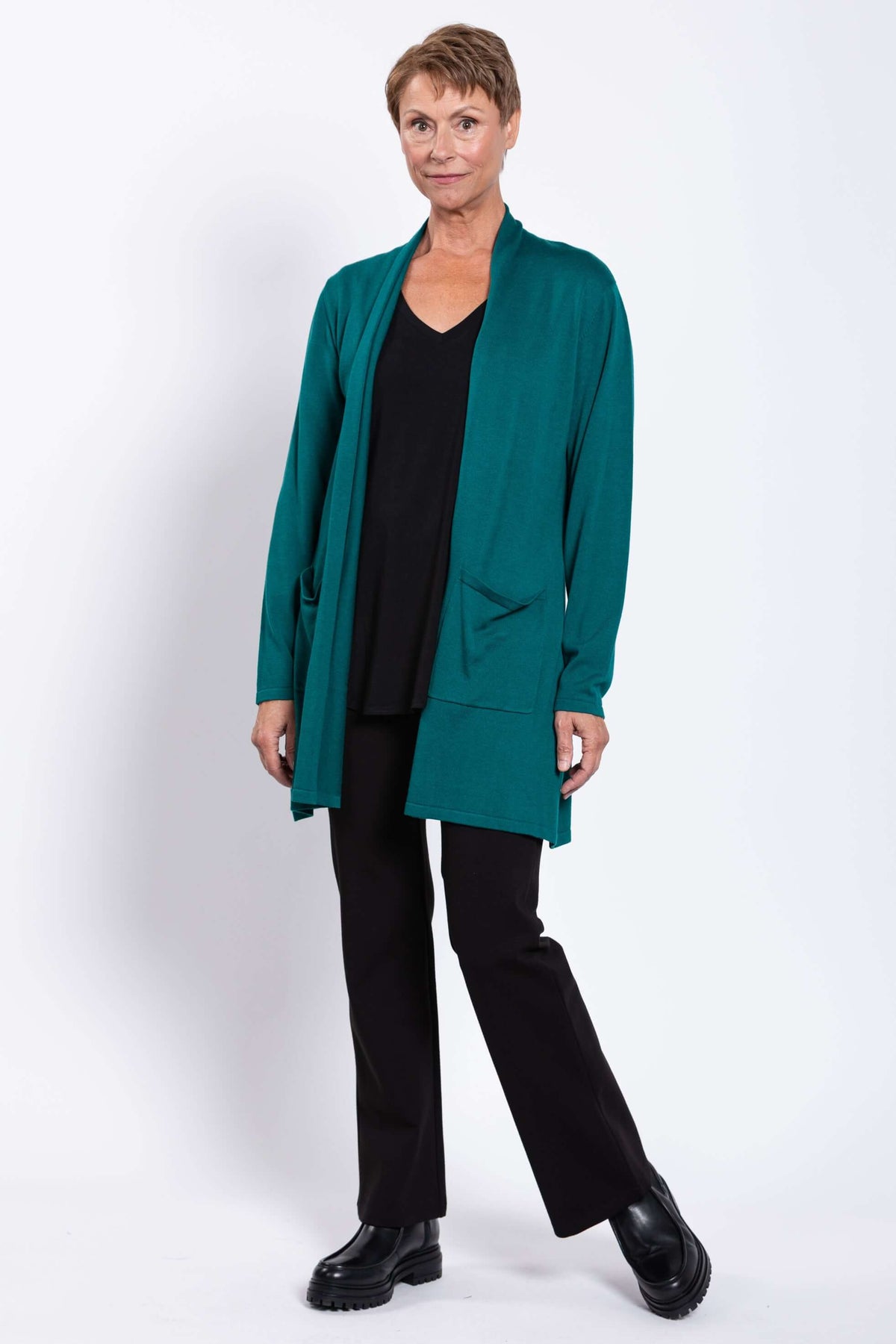 Woman in teal cardigan and black pants standing with relaxed posture