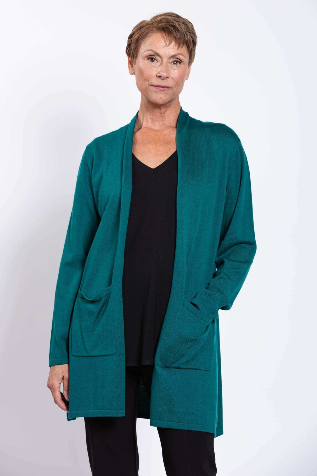 Woman in teal cardigan with hands in pockets, black top and pants, front angle