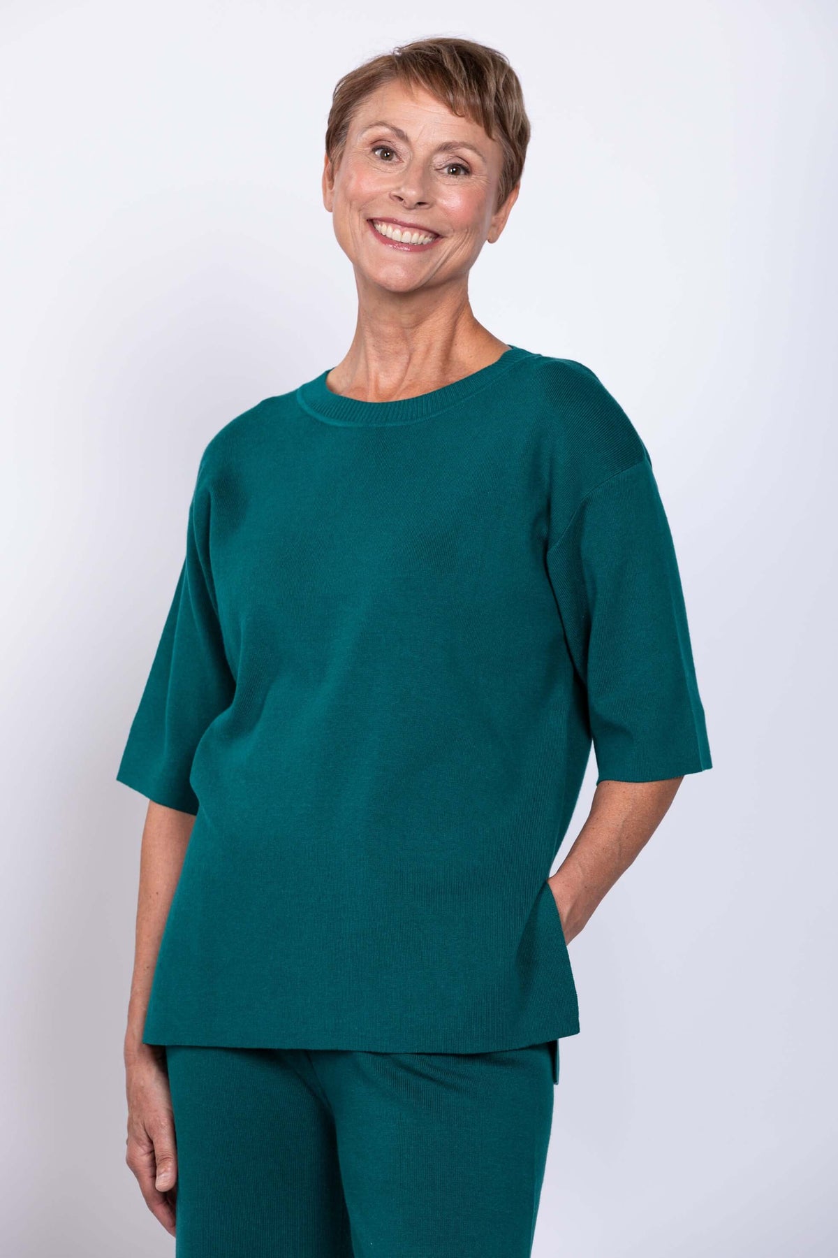 Woman in teal sweater and pants set, hand in pocket, smiling, front view