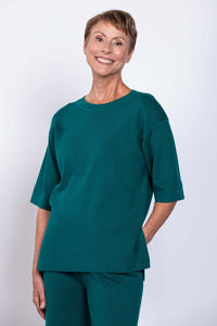Woman in teal sweater and pants set, hand in pocket, smiling, front view