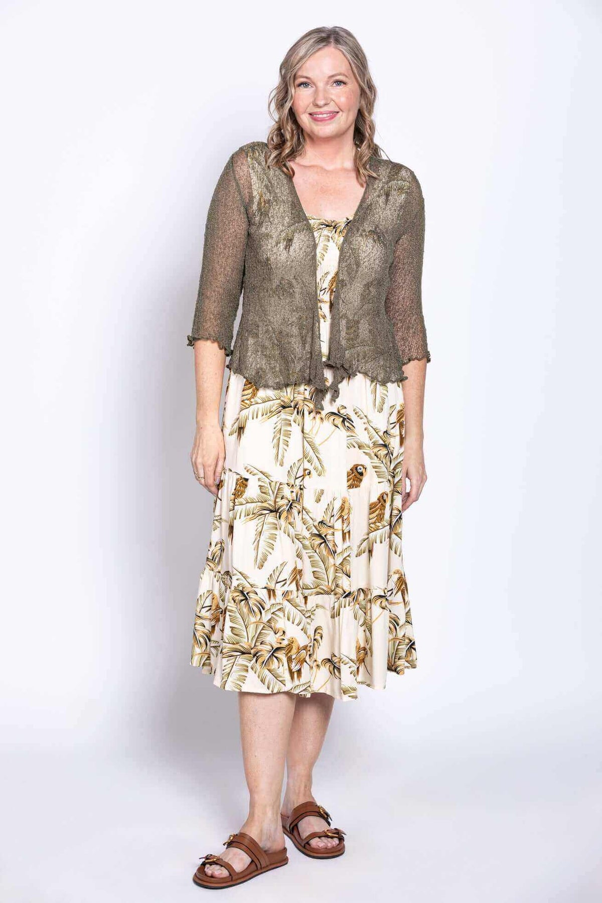 Woman layering olive mesh cardigan over tropical print dress, standing front facing