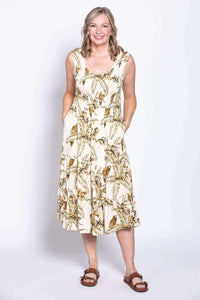 Woman in sleeveless tropical print midi dress with hands in pockets, smiling front facing