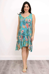Woman in turquoise sleeveless tropical floral dress standing on wood floor, smiling