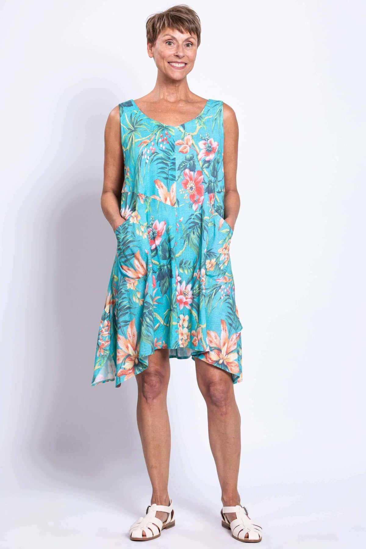 Woman wearing turquoise sleeveless dress with pink tropical floral pattern, hands in pockets