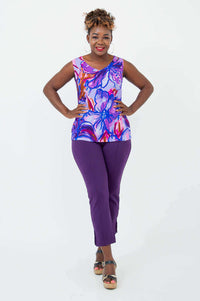 Woman posing in a vivid floral V-neck tank top and purple pants, hands on hips