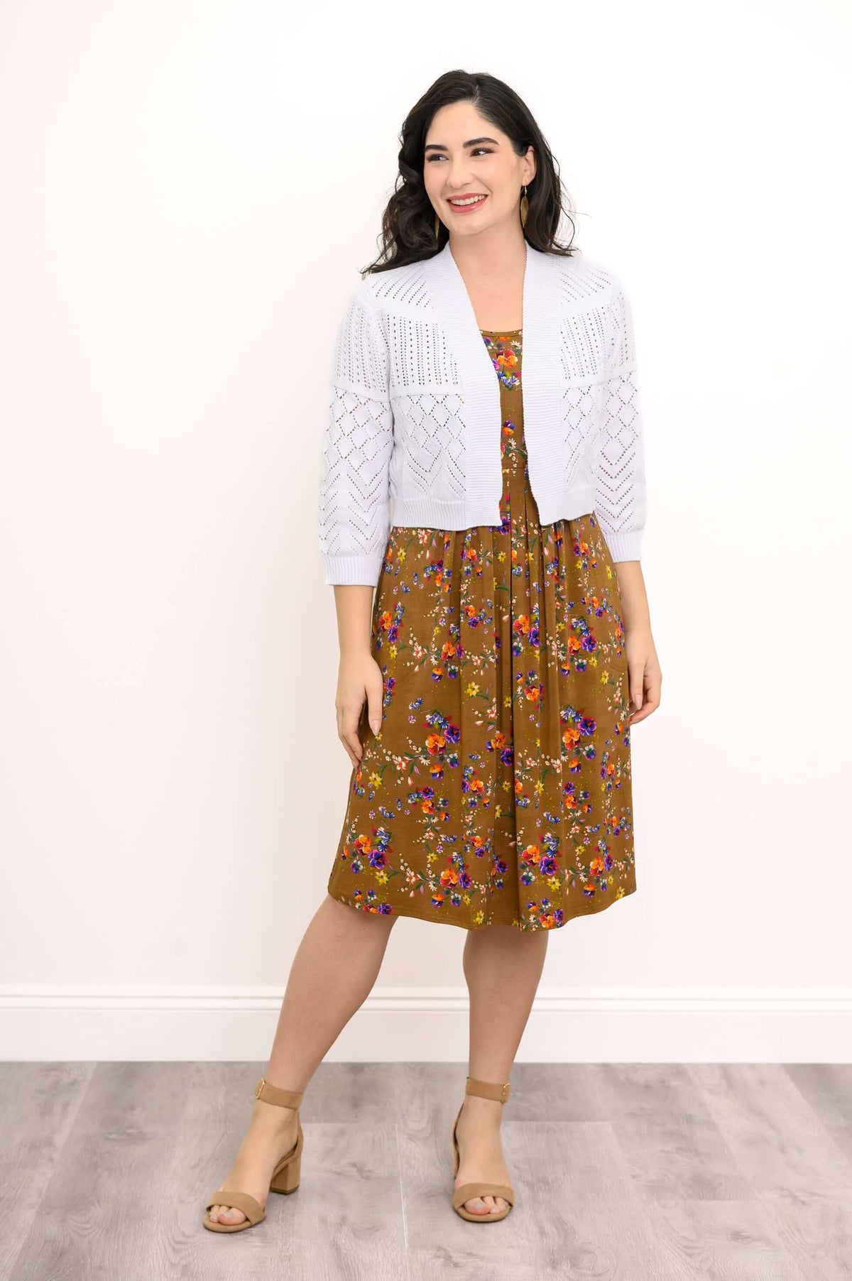 Woman standing in white knit cardigan and brown floral midi dress, smiling