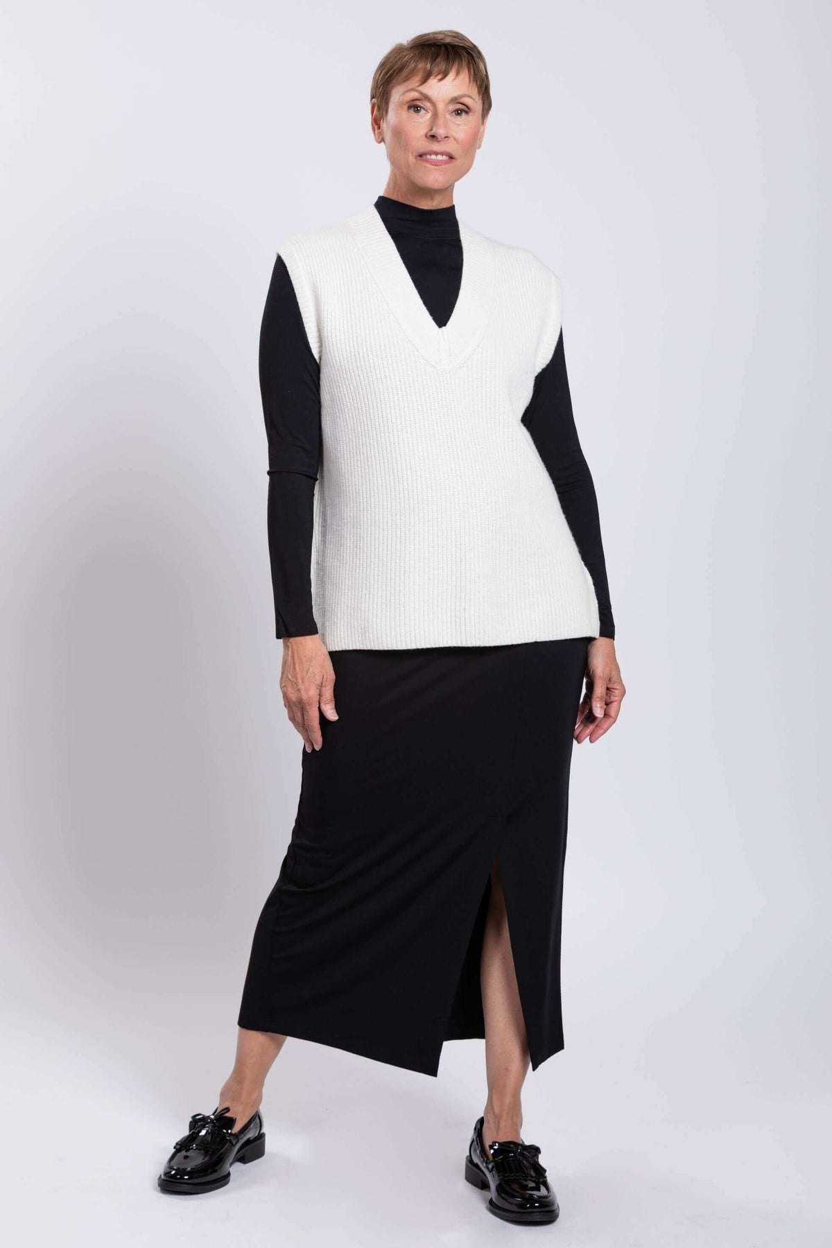 Woman in white oversized sweater vest posing with relaxed stance in studio