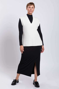 Woman in white oversized sweater vest posing with relaxed stance in studio