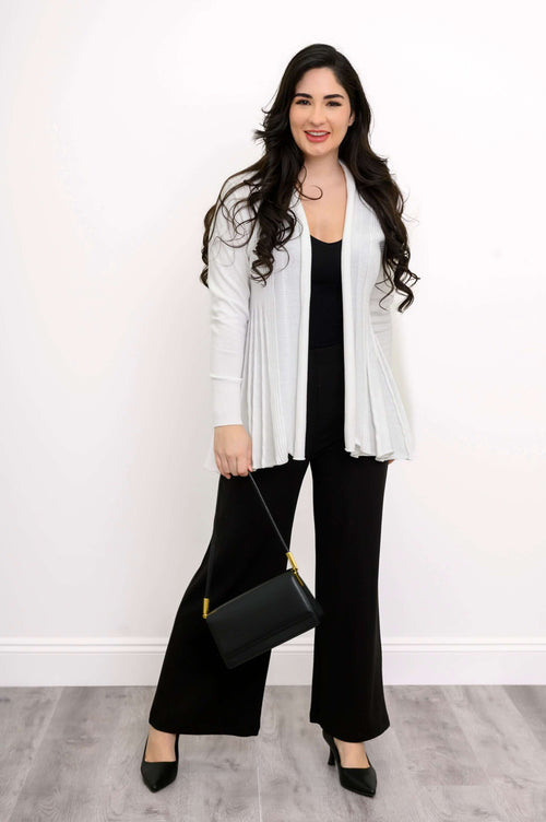 Woman in white pleated cardigan and black pants holding a black handbag