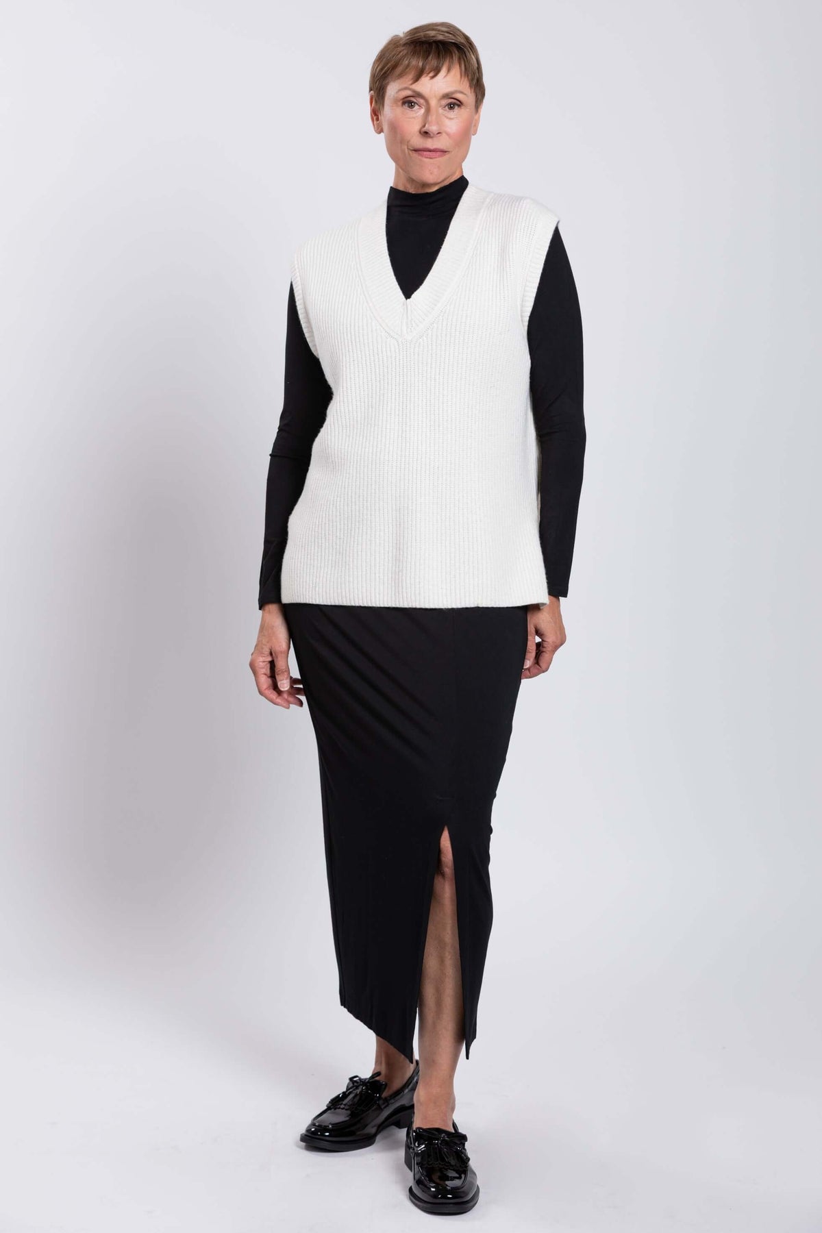 Woman in white sweater vest showing side angle with front slit skirt and black shoes