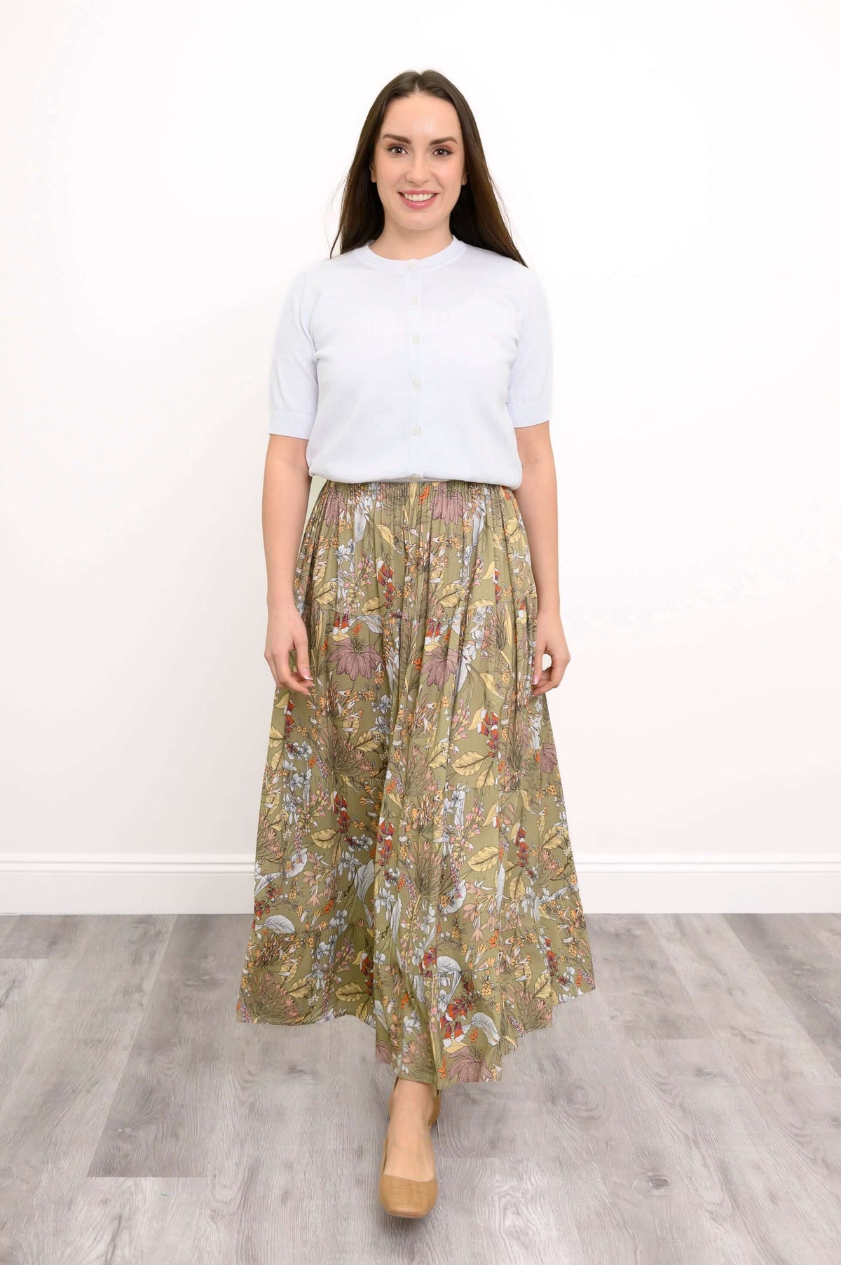 Woman wearing a white top and floral tiered maxi skirt, standing on wooden flooring