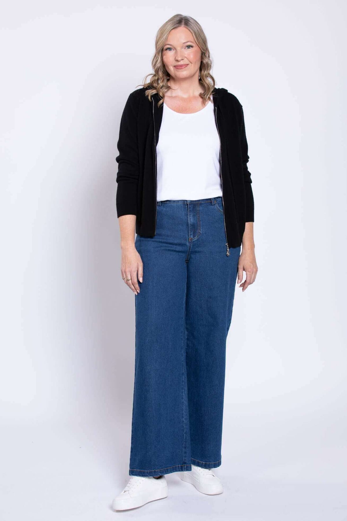 Front view of woman in wide leg blue jeans, white shirt, and black hoodie