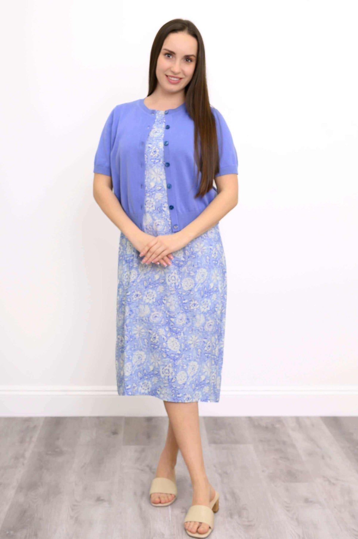 Woman layered in a blue buttoned shrug over a light blue floral midi dress