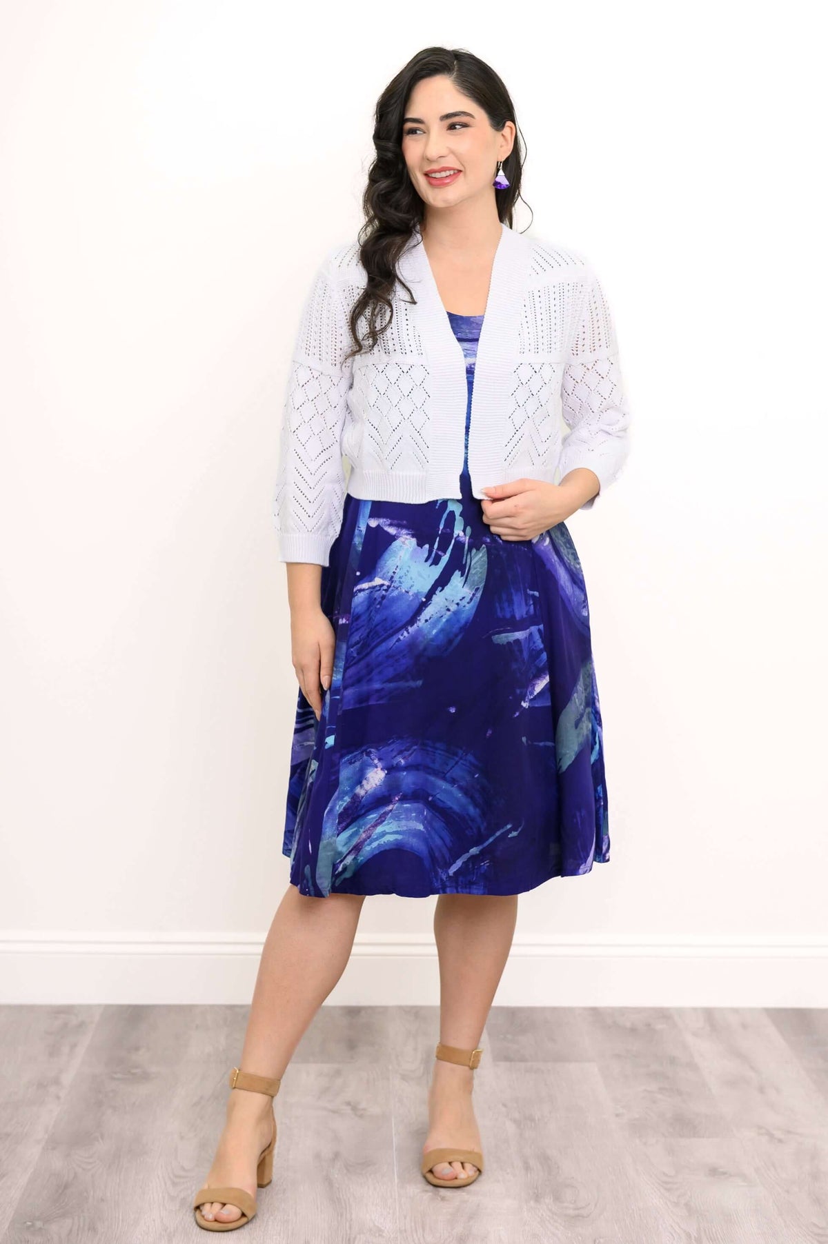 Woman layering a white knit cardigan over a blue swirl sleeveless dress