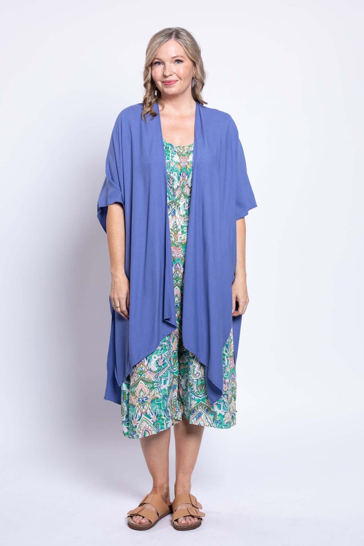 Woman wearing a blue open cardigan over a green paisley jumpsuit with tan sandals