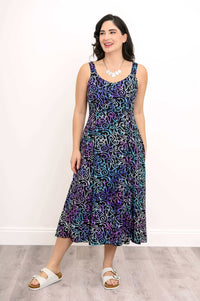 Woman in a patterned A-line dress looking to the side, hands in pockets