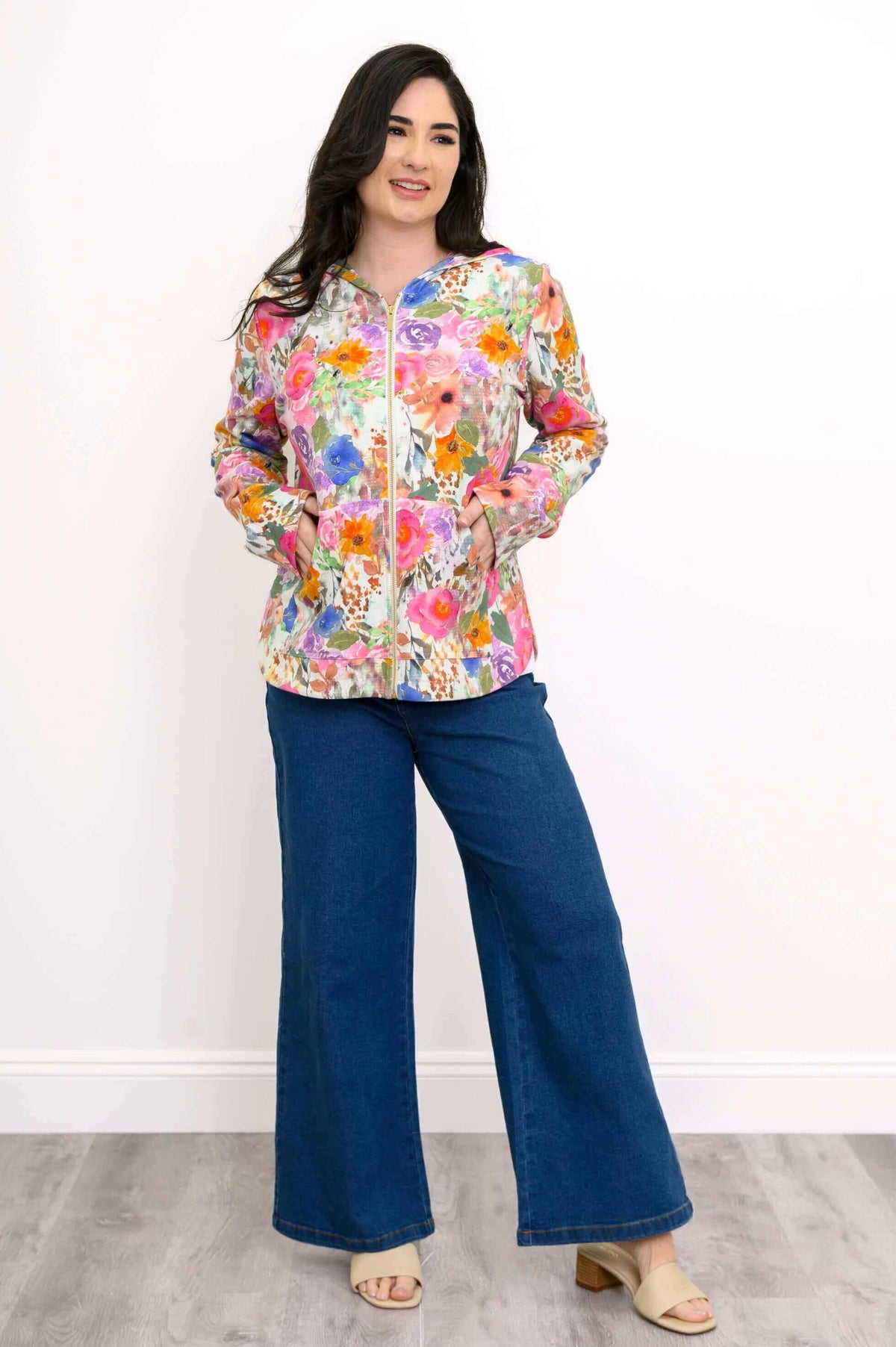 Woman with hands in pockets, wearing a pink floral hoodie and wide-leg jeans, smiling