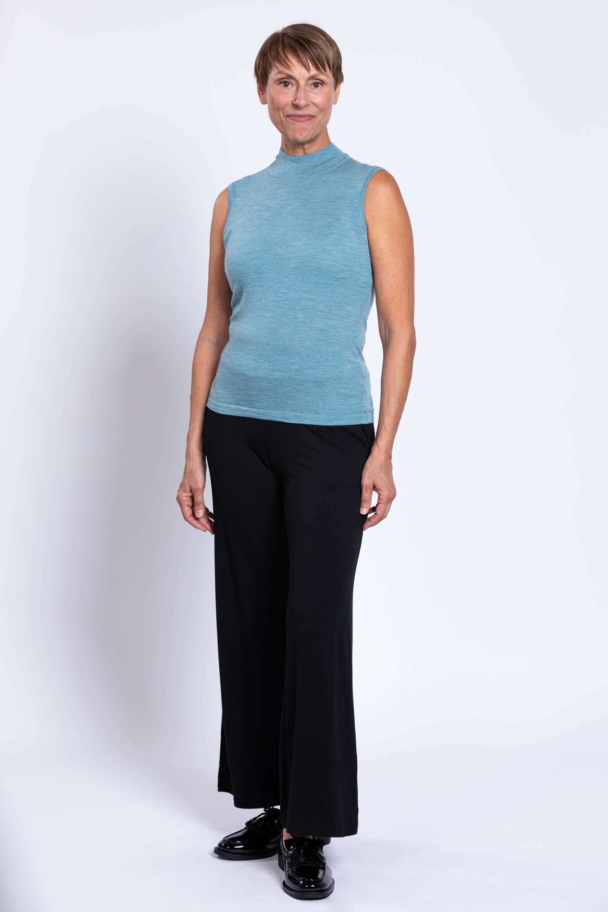 Woman modeling a blue sleeveless merino sweater with black pants and loafers
