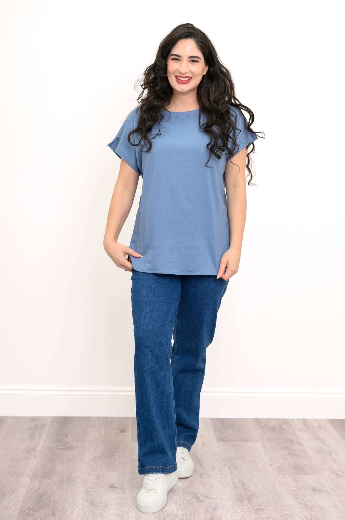 Front view of woman wearing blue cap sleeve tee and jeans on a wooden floor