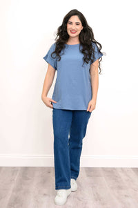 Front view of woman wearing blue cap sleeve tee and jeans on a wooden floor