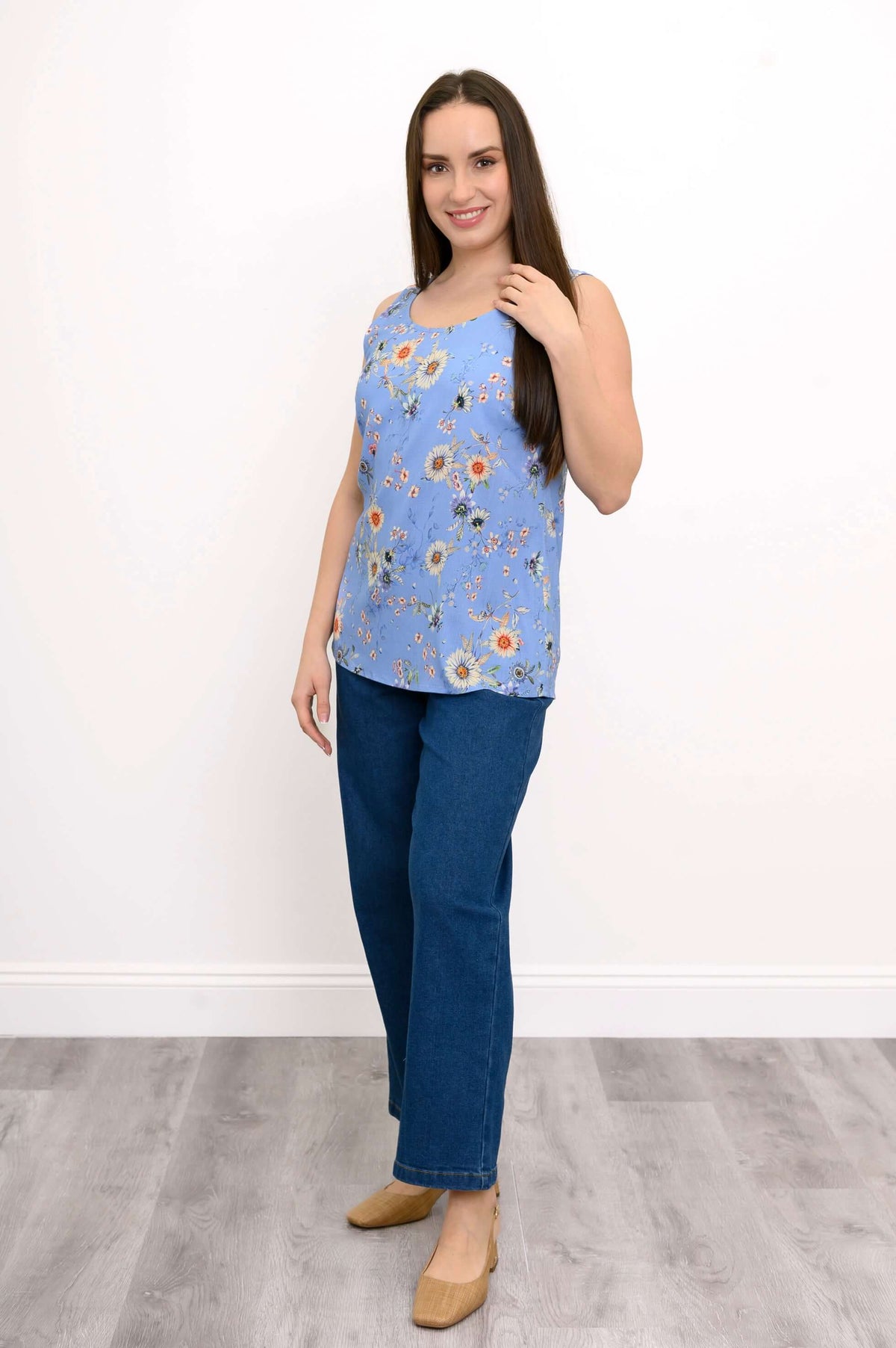 Woman posing in a blue floral tank top with jeans and tan heels