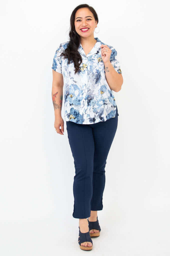 Woman smiling, modeling floral blue linen bamboo shirt and navy pants, standing front-facing