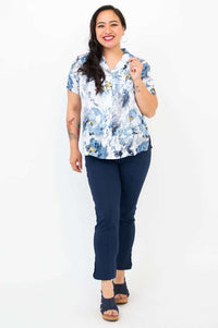 Woman smiling, modeling floral blue linen bamboo shirt and navy pants, standing front-facing