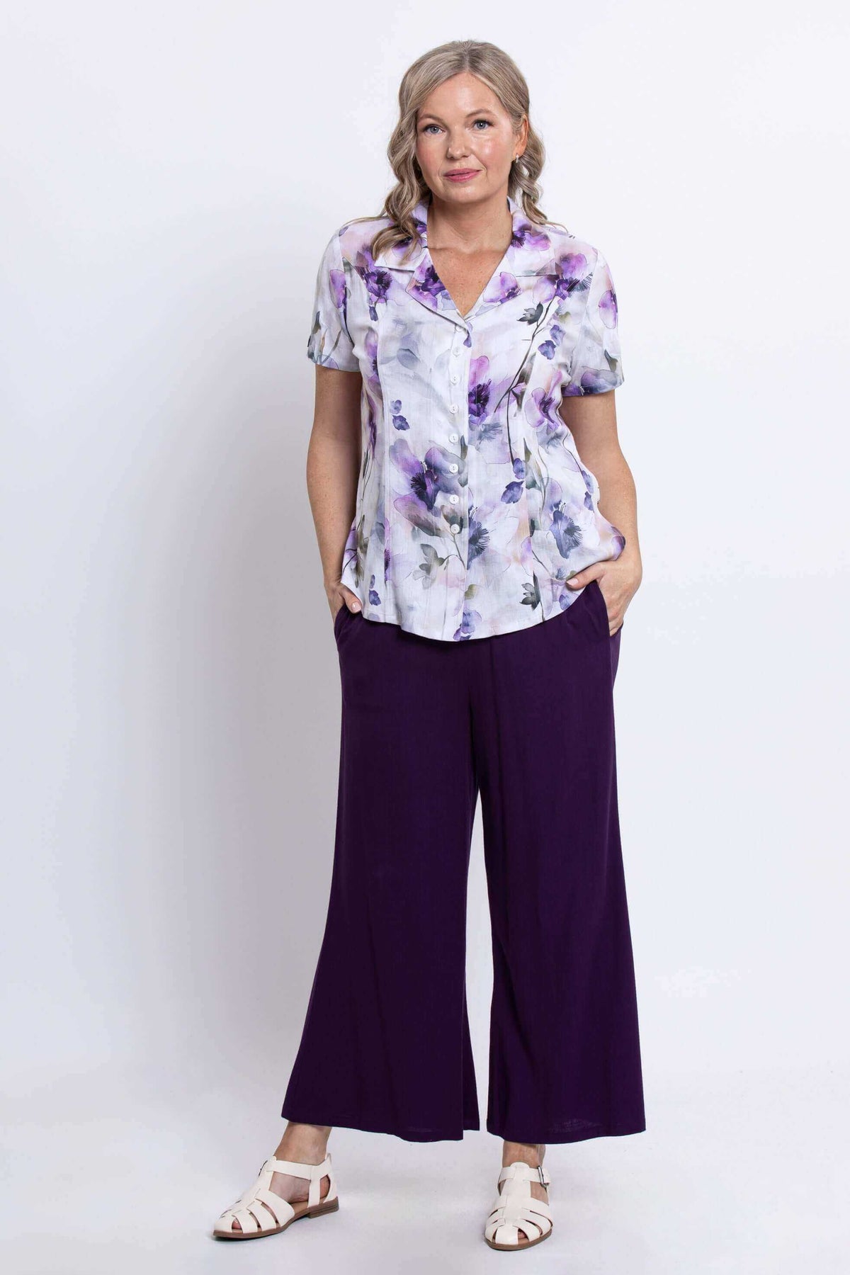 Woman modeling floral short-sleeve blouse and purple pants, hands in pockets, full body