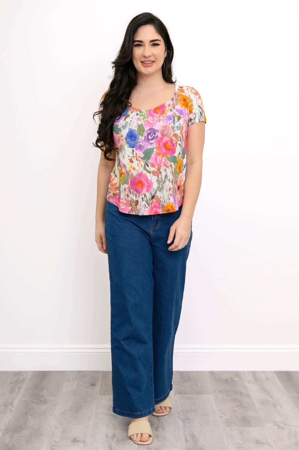 Woman in floral sweetheart top and jeans standing against white background