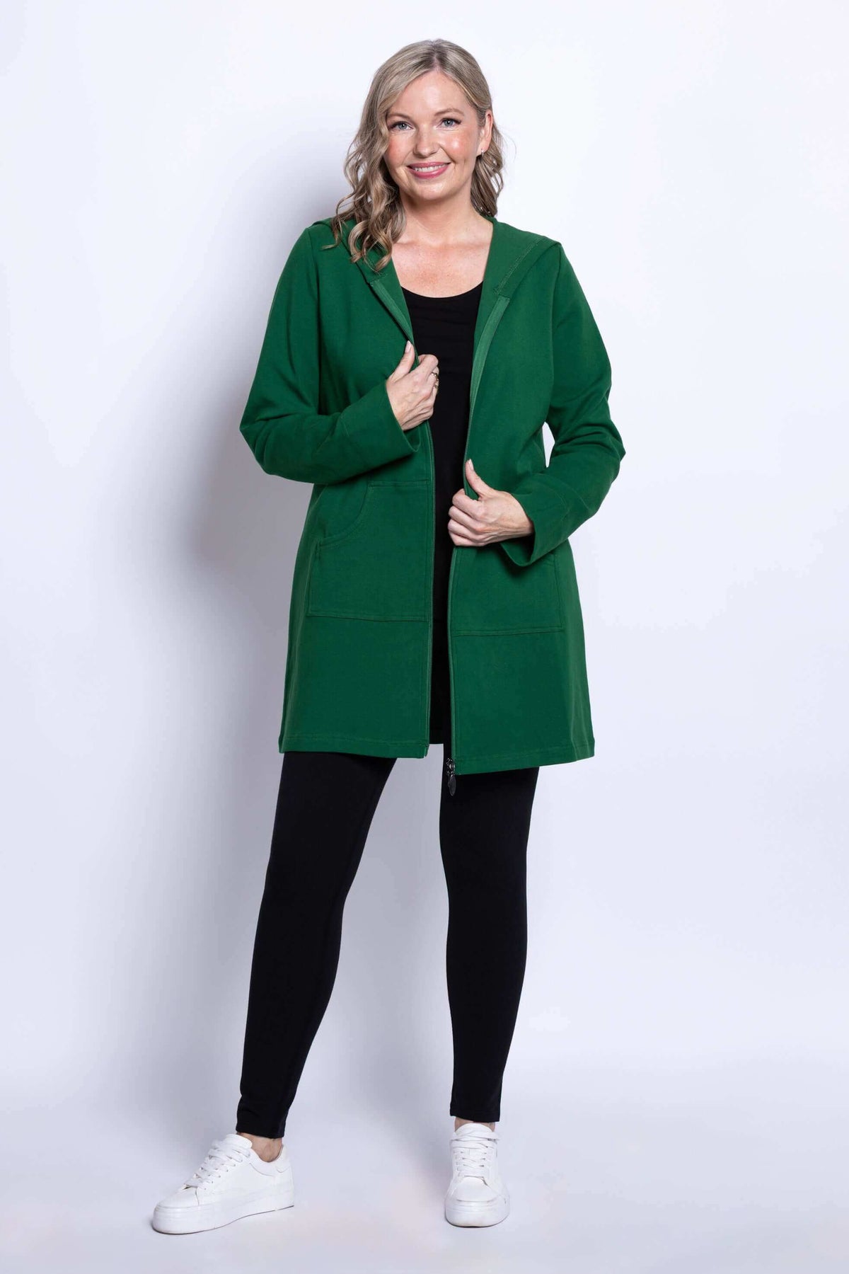 Woman smiling in green hooded jacket, unzipped over black outfit, front view