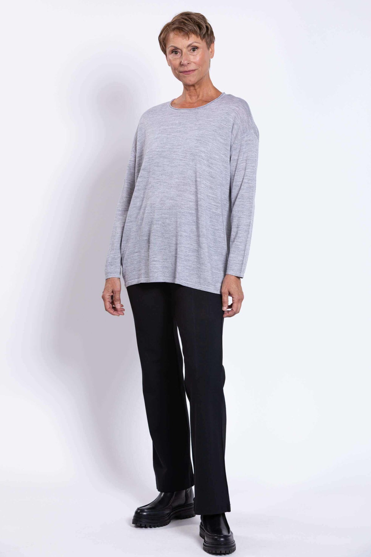 Woman modeling light grey merino sweater and black pants, facing slightly sideways