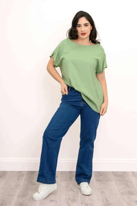 Woman posing in a light green rounded boatneck tee with casual blue jeans