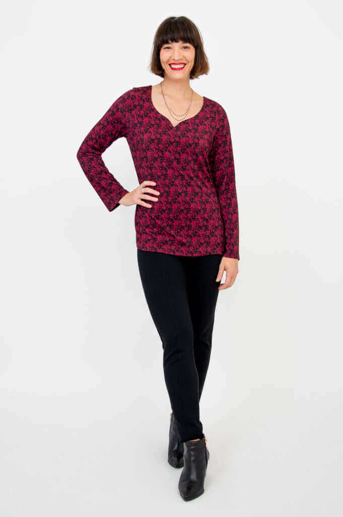 Woman in maroon floral long sleeve top and black pants, standing confidently
