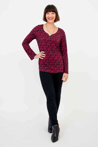 Woman in maroon floral long sleeve top and black pants, standing confidently