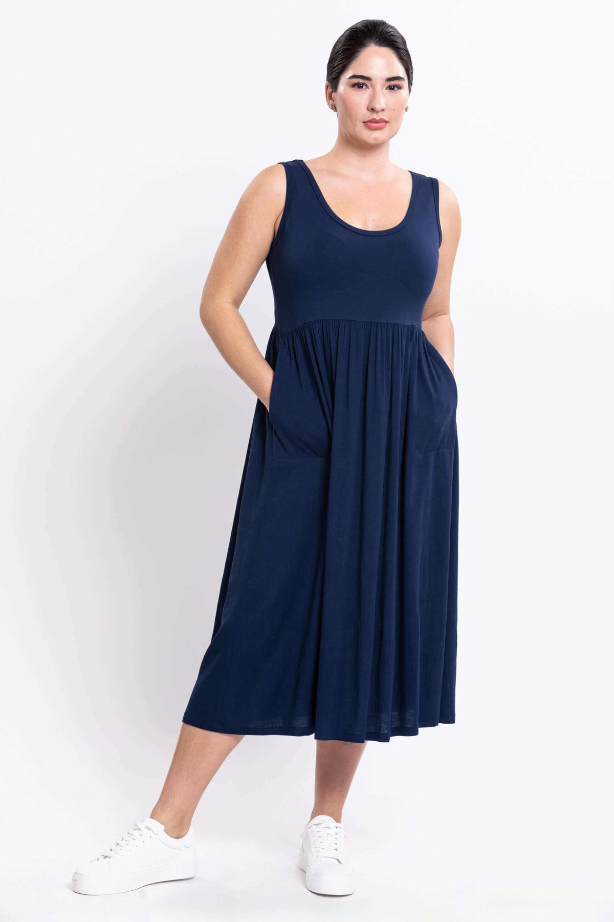 Woman in navy empire midi dress with pockets, hands in pockets, front view