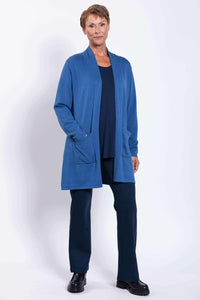 Woman standing in a blue cardigan, hand in pocket, showcasing relaxed fit